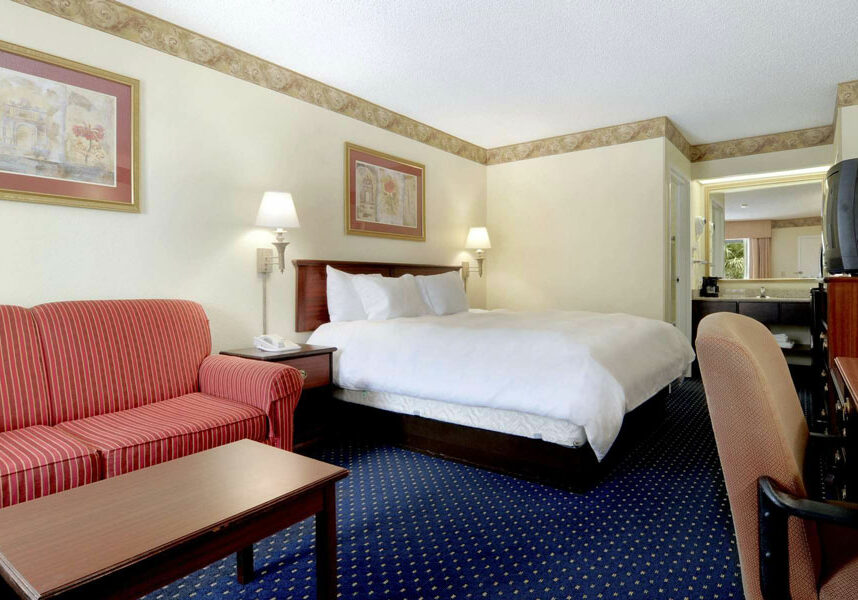 one guest bed room with plush bed, striped sofa, work desk with chair, TV, and coffee table at Baymont by Wyndham Tallahassee