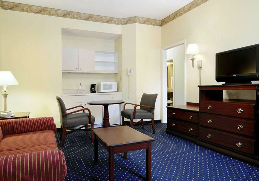 suite living area with striped sofa, coffee table, table with two chairs, dresser, flat screen TV, microwave, coffee maker, and sink at Baymont by Wyndham Tallahassee